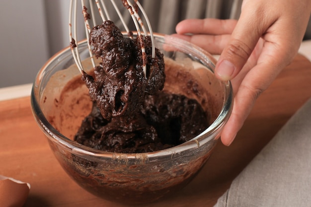 Mezcla de chocolate derretido y cacao en polvo en un tazón grande para hacer masa / mezcla / masa para un delicioso pastel de brownie casero en una mesa de madera, usando un batidor de bolas