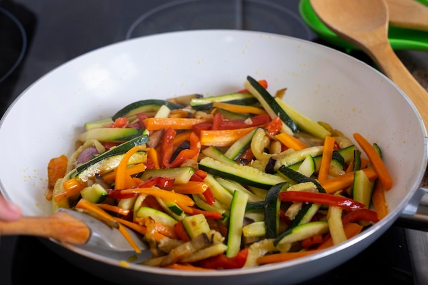 Mezcla coloreada de verduras frescas fileteadas calabacines zanahorias pimientos y berenjenas salteadas en una sartén
