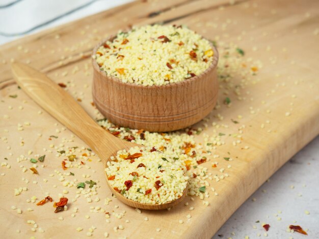 Mezcla de cuscús con especias y tomates en un tazón de madera y un primer plano de cuchara