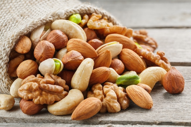 Mezcla de diferentes nueces en una taza de madera sobre el fondo de tela de arpillera