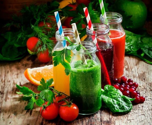 Mezcla de jugos de frutas y verduras saludables en botellas pequeñas con pajitas de rayas de colores enfoque selectivo de fondo de madera vieja