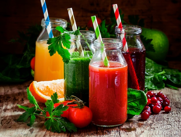 Mezcla de jugos de frutas y verduras saludables en botellas pequeñas con pajitas de rayas de colores enfoque selectivo de fondo de madera vieja