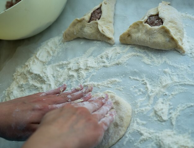 Mezcla de masa. Concepto de peremech para hornear. Ingredientes para cocinar harina, masa y carne. Vista superior de las manos de cocinar cocinas belyash. carne molida con agujero