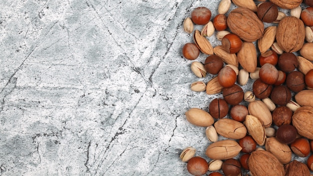 Mezcla de nueces con cáscara crudas sobre fondo de piedra gris.