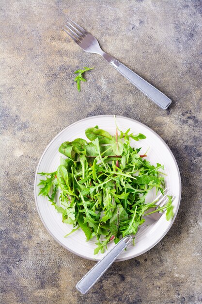 Una mezcla de rúcula fresca, acelgas y hojas de mizun en un plato y tenedores sobre la mesa. alimentación saludable. Vista superior y vertical