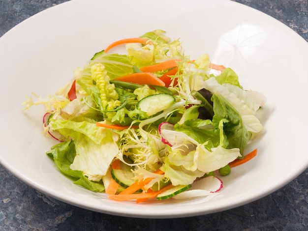 Mezcla de sabrosa ensalada de verduras frescas en una placa blanca sobre un fondo gris