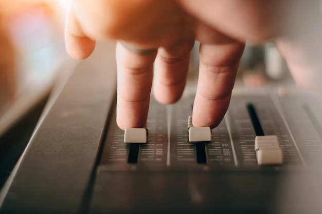 Mezclador de sonido de escenario profesional de cerca en la mano del ingeniero de sonido usando el control deslizante de mezcla de audio trabajando durante la actuación de concierto. DJ está ajustando el volumen del sonido