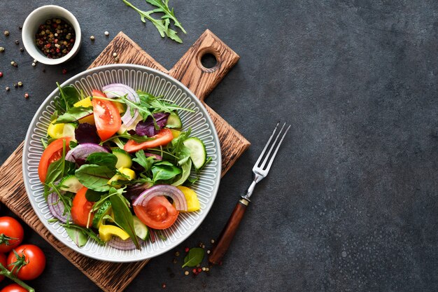 Mezclar la ensalada con tomate, cebolla y aceite de oliva en un plato sobre una tabla de madera sobre un fondo de hormigón negro.