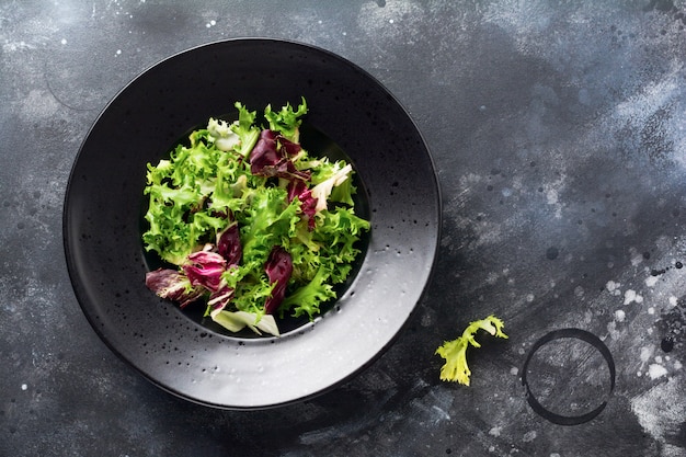 Mezcle hojas frescas de rúcula, lechuga, espinaca, remolacha para ensalada sobre un fondo de piedra oscura. Enfoque selectivo.