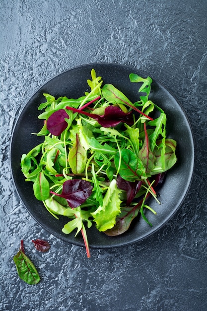 Mezcle hojas frescas de rúcula, lechuga, espinaca, remolacha para ensalada sobre una superficie de piedra oscura.