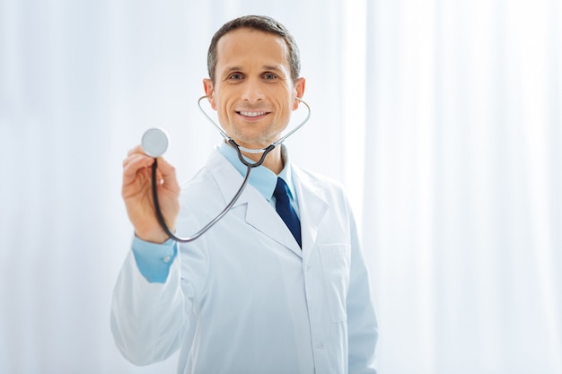 Foto mi gadget. médico profesional manteniendo una sonrisa en su rostro y sosteniendo un estetoscopio