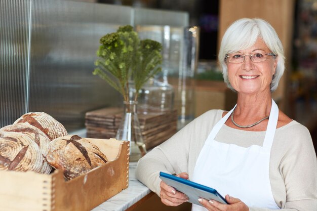 Para mí, la herramienta de administración de pequeñas empresas más inteligente Retrato de una anciana feliz que usa una tableta digital para administrar su panadería