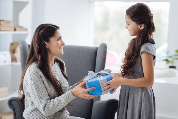 De mi hija. Encantado de atractiva mujer agradable mirando a su hija y sonriendo mientras recibe un regalo de ella