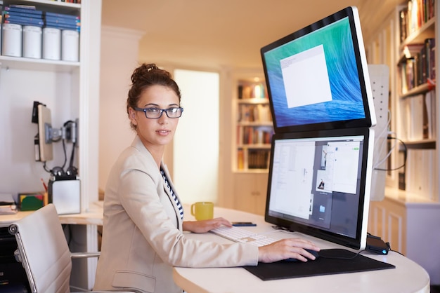 Mi pantalla dual me da mayor productividad Retrato de una mujer joven que trabaja en una computadora de pantalla dual en casa