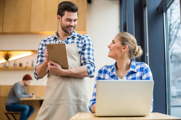 Mi pedido. Alegre mujer agradable positiva sentada en la mesa y hablando con el camarero mientras hace un pedido en el café