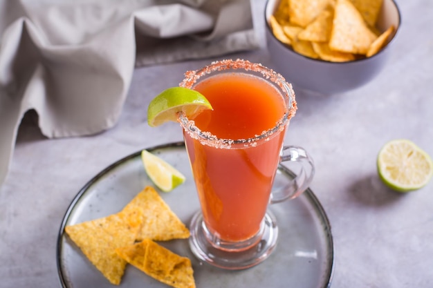 Michelagua-Mocktail mit Tomatensaft und Limettensaft in einem Glas und Nachos in einer Schüssel