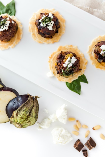 Micro Bruschetta de Caponata de Berenjena de Chocolate con Vinagre Balsámico de Chocolate y Aperitivos de Queso de Cabra de Montaña de Pajar Desmenuzado.