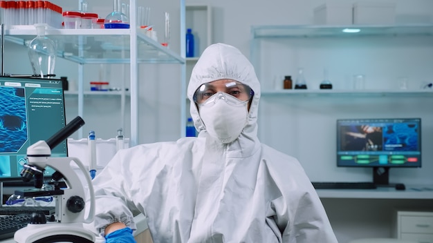 Microbiologista cansado de macacão sentado no laboratório, olhando para a câmera. Equipe de cientistas examinando a evolução do vírus usando ferramentas de alta tecnologia e química para pesquisa científica e desenvolvimento de vacinas.