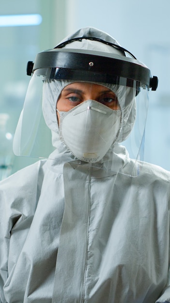 Microbiólogo cansado en mono sentado en laboratorio mirando a cámara. Equipo de científicos que examinan la evolución del virus utilizando herramientas de alta tecnología y química para la investigación científica y el desarrollo de vacunas.