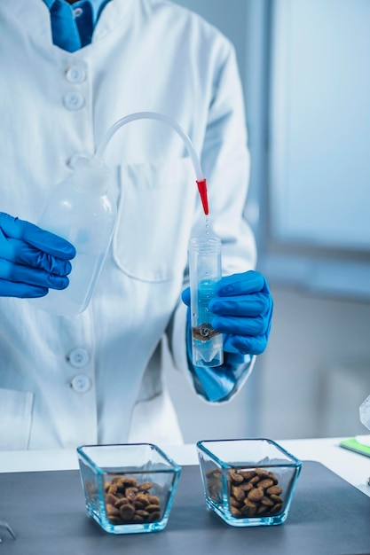 Microbiólogo de laboratorio de pruebas de alimentos para mascotas vertiendo agua en un tubo de ensayo con muestras de alimentos secos para mascotas