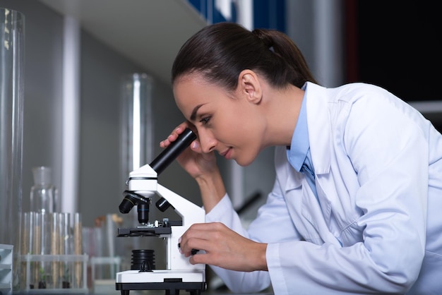 Microbiólogos realidad Adulto lindo científico razonable en un uniforme de pie en el laboratorio trabajando con el microscopio y mirando en el alcance