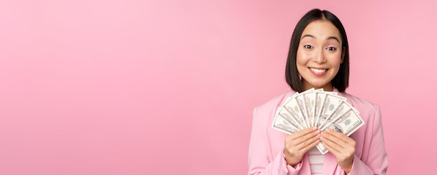 Microcrédito financeiro e conceito de pessoas Feliz empresária asiática sorridente mostrando dinheiro em pé de terno contra fundo rosa