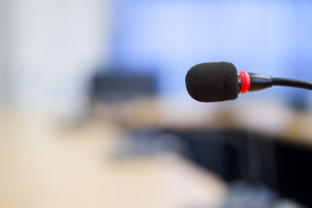 Microfones de conferência em close-up em uma sala de reuniões estão desfocados no fundo.