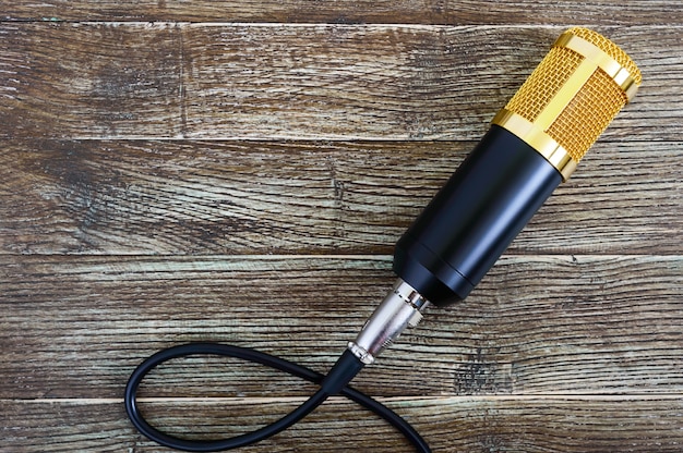 Foto micrófono de condensador dorado con cable sobre una mesa de madera con espacio de copia. tema musical. endecha plana. vista superior.