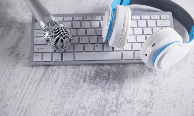 Micrófono, teclado y auriculares en un escritorio blanco.