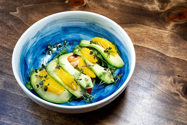 Microgreen auf einem Avocado-, Garnelen- und Orangensalat in einem blauen Teller. Tisch für Foto- und Videoaufnahmen.