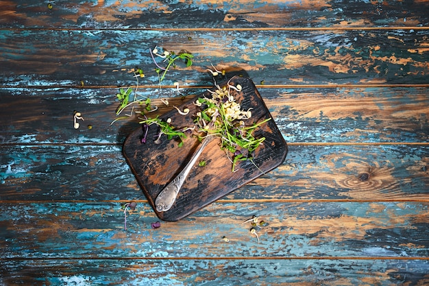 Microgreen en tenedor antiguo en tablero de cocina quemado en mesa azul de madera teñida en bruto.