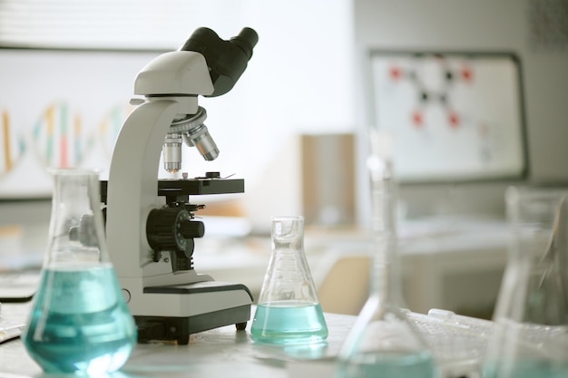 Un microscopio moderno instalado en un laboratorio rodeado de vasos de vidrio llenos de líquidos de colores