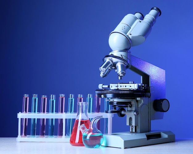 Microscopio y tubos de ensayo en la mesa sobre un fondo de color