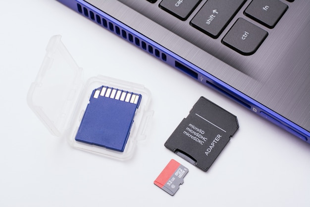 MicroSD-Speicherkarte mit Adapter in der Nähe des SD-Anschlusses des modernen blauen Laptops. Eine weitere blaue SD-Speicherkarte in einer transparenten Hülle befindet sich in der Nähe des Computers.