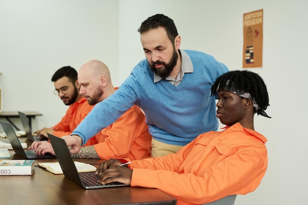 Middle aged caucasian man instructing diverse young adults using laptops