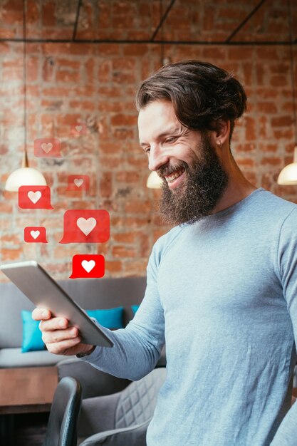 Foto mídias sociais como feedback positivo comunicação online global blogueiro masculino hipster sorridente usando tablet com ilustração de ícones de coração no interior do loft