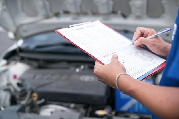 Midsection de mecânico escrevendo em clipboard enquanto estava de pé pelo carro