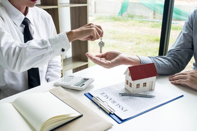 Foto midsection do agente dando a chave ao proprietário na mesa no escritório