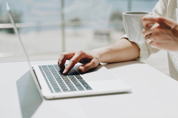 Midsection eines Mannes, der einen Laptop benutzt, während er Kaffee auf dem Tisch trinkt