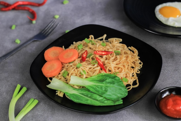 Mie Goreng Gebratene Nudeln, serviert mit Spiegeleiern und Gemüse auf einem Teller