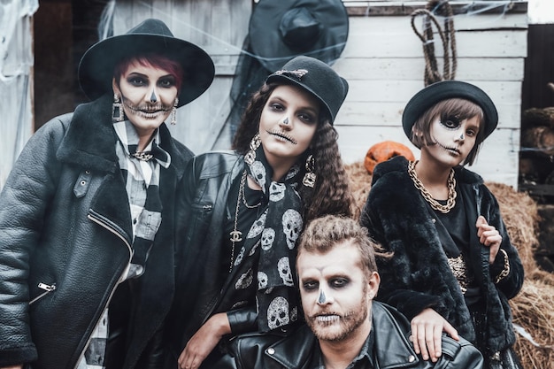 Miedo familia madre padre hijas celebrando Halloween Terrorífico maquillaje de media cara de calavera negra y disfraces de brujas imágenes elegantesHorrorfun at children's party in barn on streetSombreroschaquetas