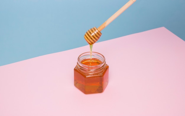 La miel de abeja gotea de una espátula de madera en un frasco de vidrio