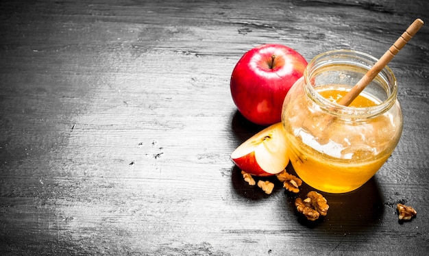 Foto miel en bote con rodajas de manzanas maduras y nueces.