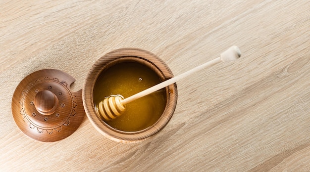 Miel con cucharón de miel de madera en un tazón de madera sobre una mesa de madera.
