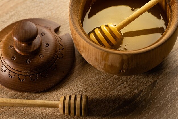 Miel con cucharón de miel de madera en un tazón de madera sobre una mesa de madera.