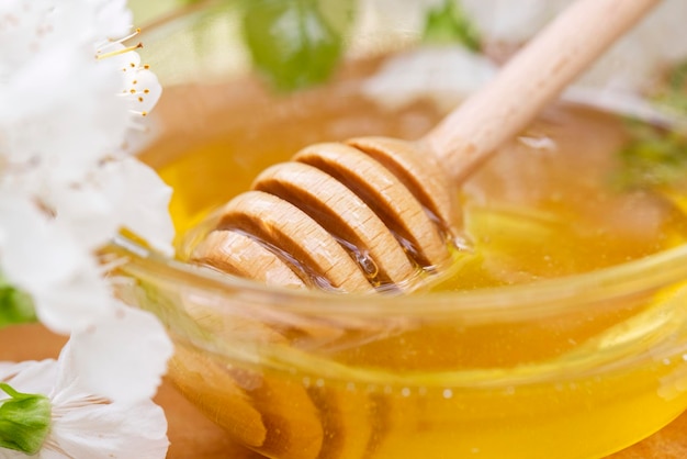 Foto la miel de flores en un cuenco de vidrio con una cuchara de miel de madera en una mesa de madera con flores