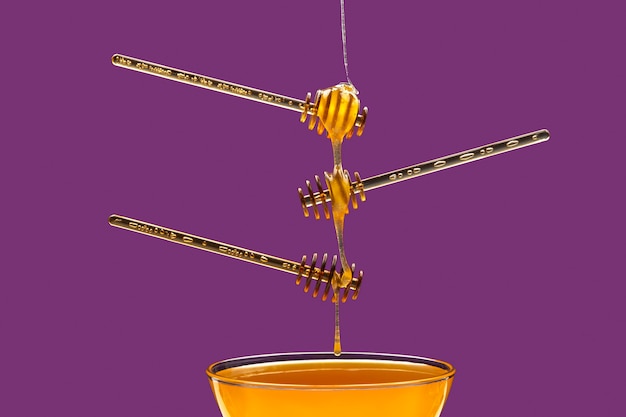 Foto la miel de flores frescas gotea de una cuchara en una cuchara sobre un fondo púrpura. alimentos vitamínicos orgánicos.
