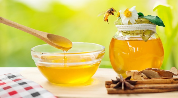 Miel en frasco de vidrio con abejas volando y flores sobre un piso de madera