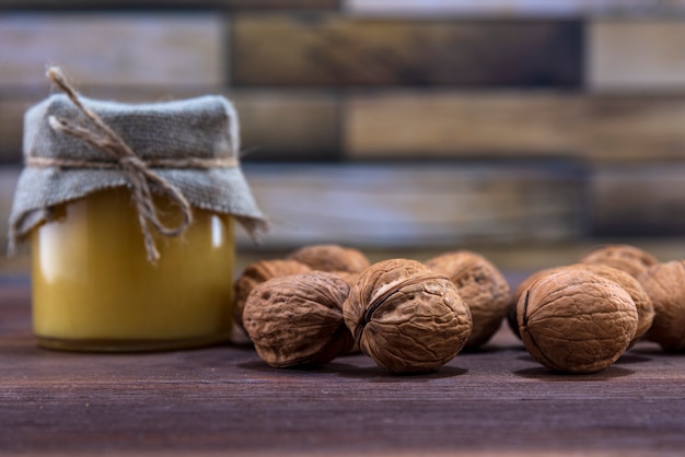 Miel en un frasco de vidrio y muchas nueces con cáscara sobre una superficie de madera