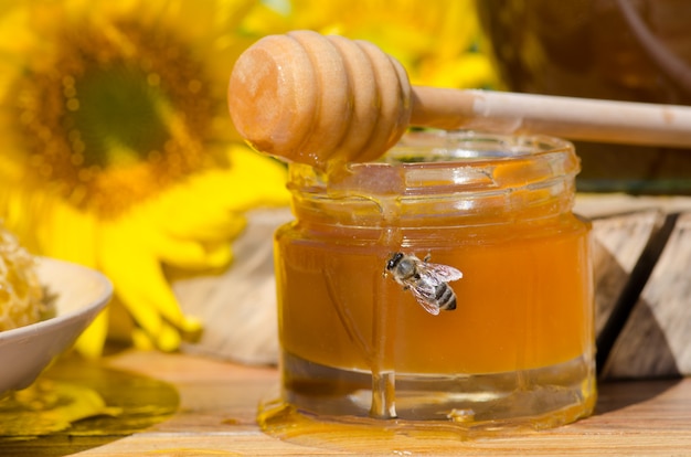 Miel en frascos de vidrio y miel de abeja occidental. Miel De Abeja. Abeja sentada en un vaso de miel. Miel en frasco de vidrio con abejas voladoras